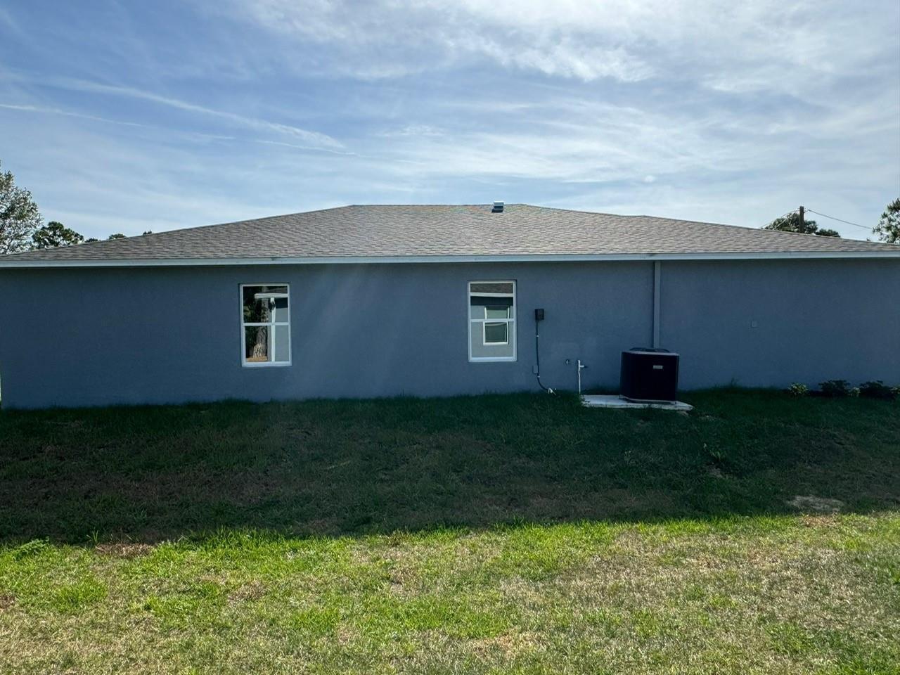 A view of the gray stucco exterior of a house with two windows and an AC unit — 6050 Pecan Circle, FL 33935, FL