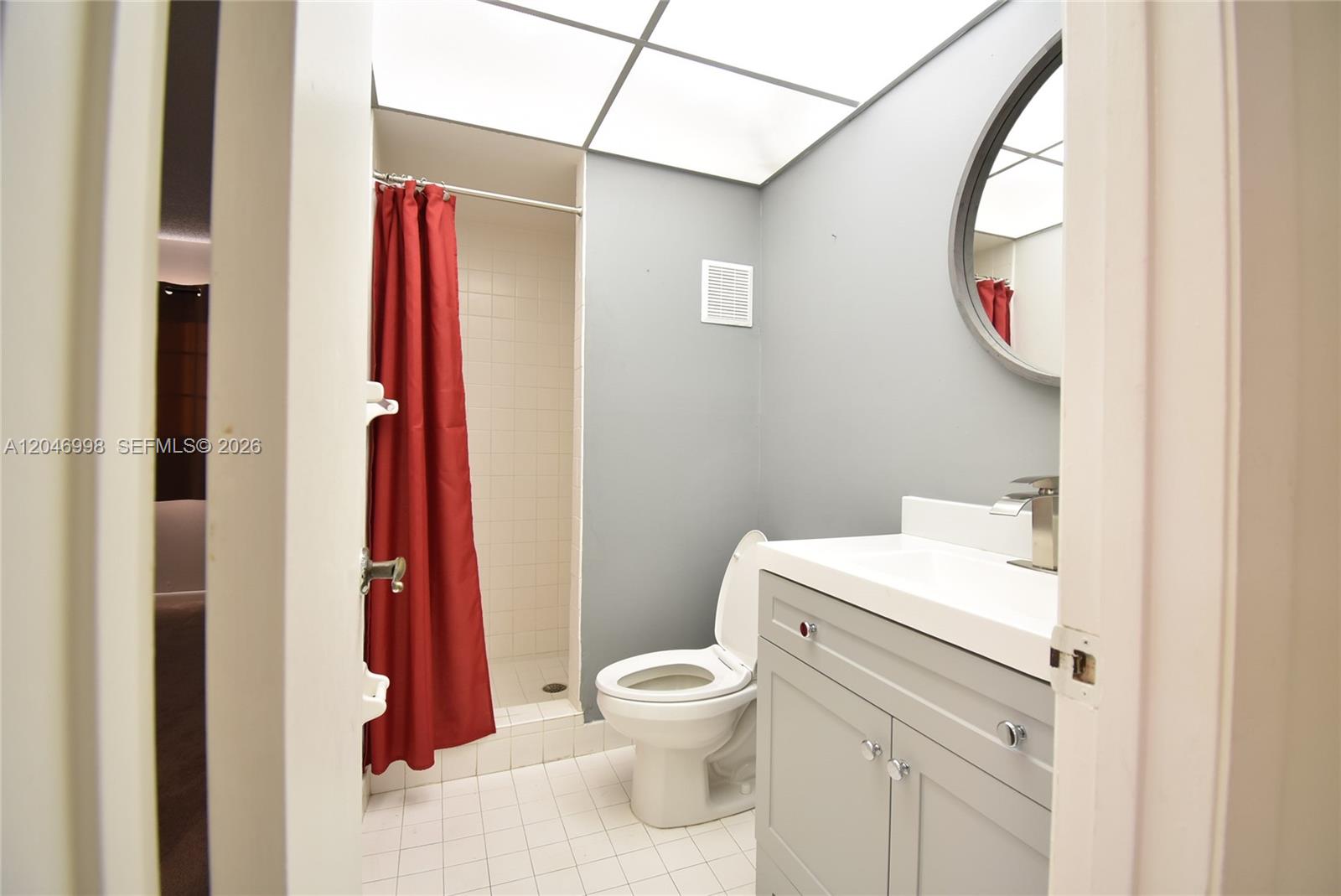 A bathroom features a gray vanity, a white toilet, and a shower with a red curtain — 20741 NE 4th Ct # 104, Miami FL 33179, MIAMI, FL