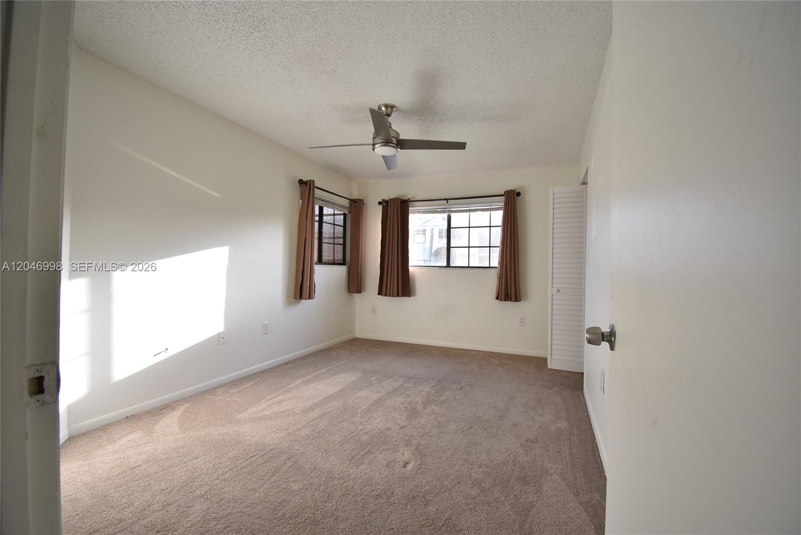 An empty bedroom features beige carpet, white walls, a ceiling fan, and two windows — 20741 NE 4th Ct # 104, Miami FL 33179, MIAMI, FL