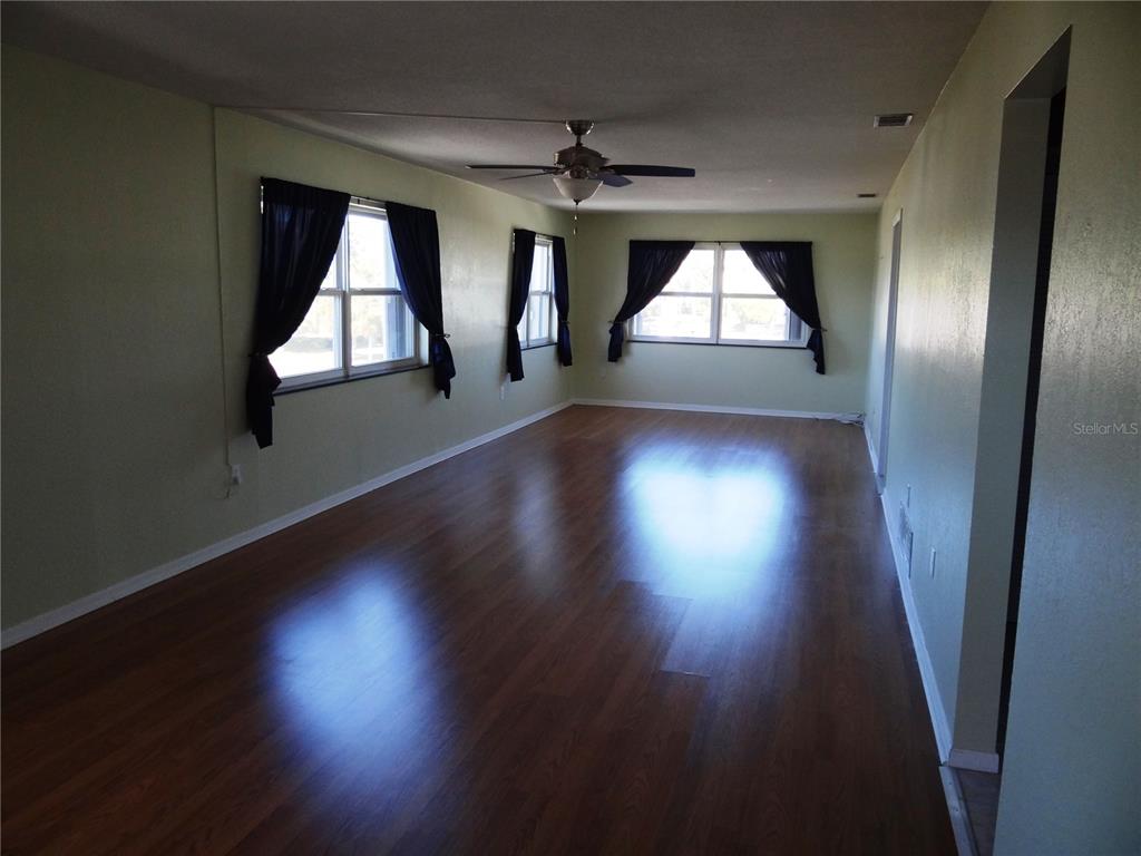 An empty room with light green walls, dark wood flooring, and several windows with curtains — 5357 81ST STREET N UNIT 14, ST PETERSBURG, FL