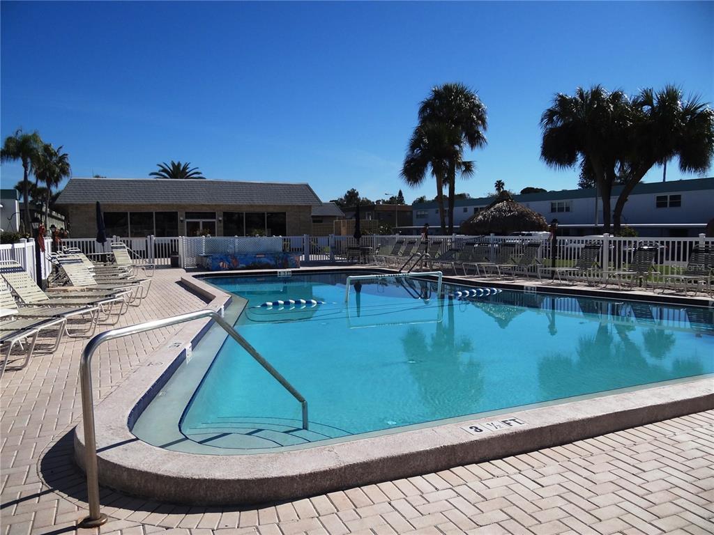An outdoor swimming pool with lounge chairs on a paved deck under a clear sky — 5357 81ST STREET N UNIT 14, ST PETERSBURG, FL
