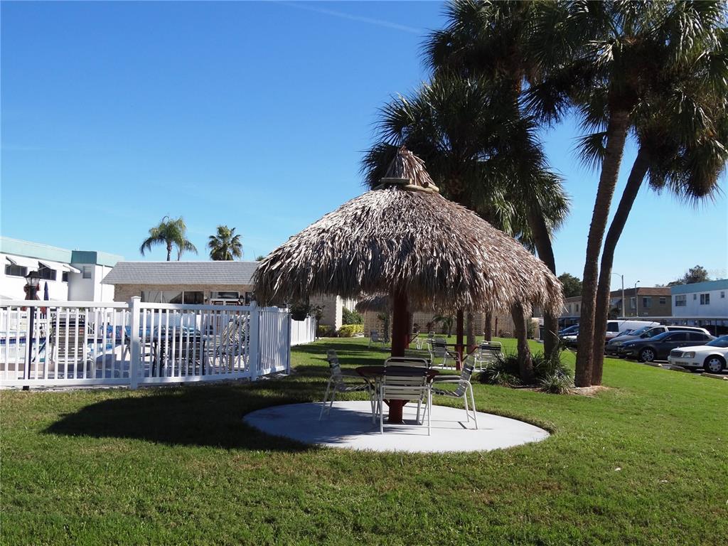 A thatched-roof tiki hut with outdoor seating sits on a concrete pad near palm trees — 5357 81ST STREET N UNIT 14, ST PETERSBURG, FL