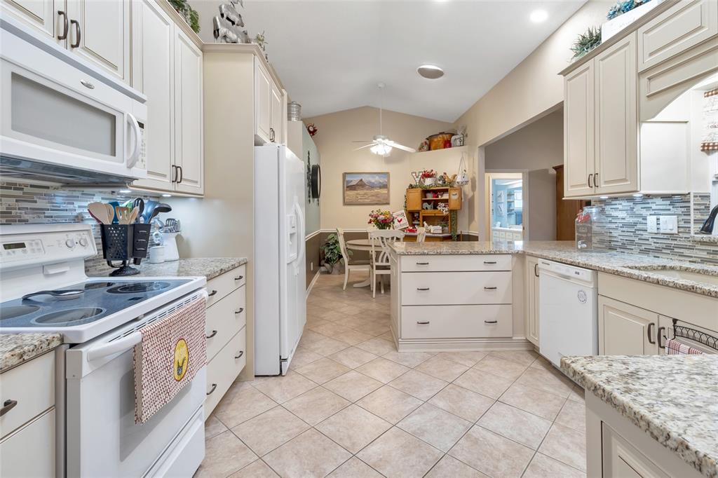 A kitchen with white cabinets, granite countertops, and a dining area in the background — 21830 KING EDWARD COURT, LEESBURG, FL