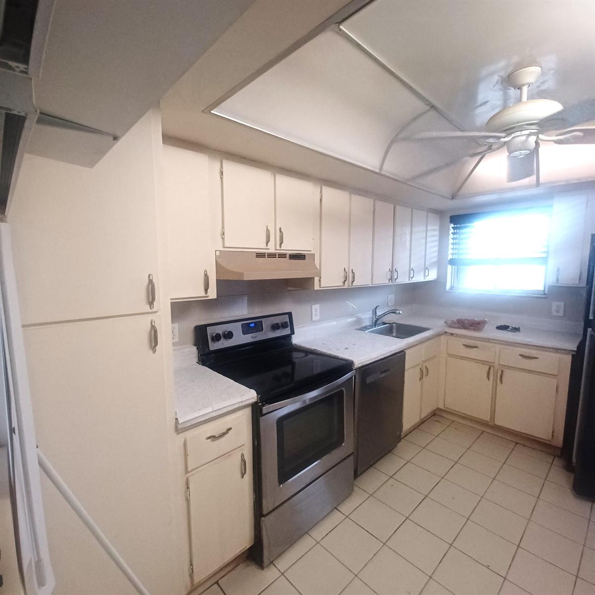 A kitchen features white cabinets, stainless steel appliances, tiled countertops, and a ceiling fan — 3186 Via Poinciana # 311, FL 33467, FL