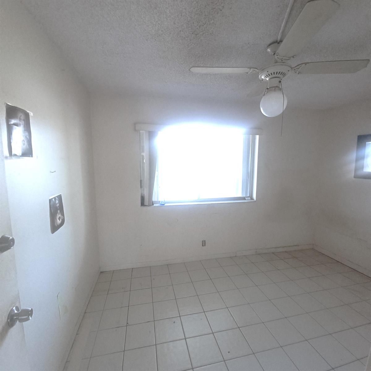 An empty room features white walls, tiled flooring, a ceiling fan, and a single window — 3186 Via Poinciana # 311, FL 33467, FL