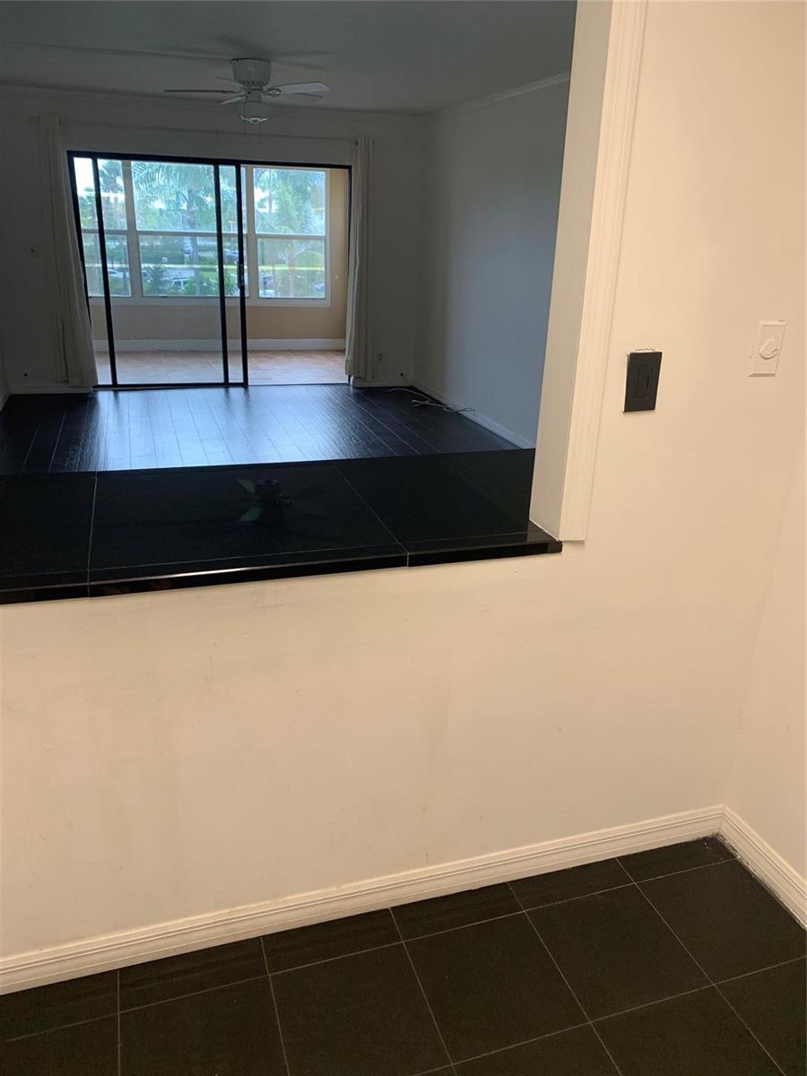 A kitchen pass-through window overlooks a living area with dark flooring and sliding glass doors — 9355 SW 8th Street # 321, Boca Raton FL 33428, BOCA RATON, FL