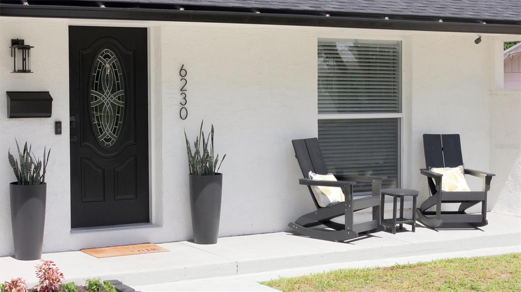 A white house exterior features a black front door, two black planters, and two chairs — 6230 CEDAR STREET NE, ST PETERSBURG, FL