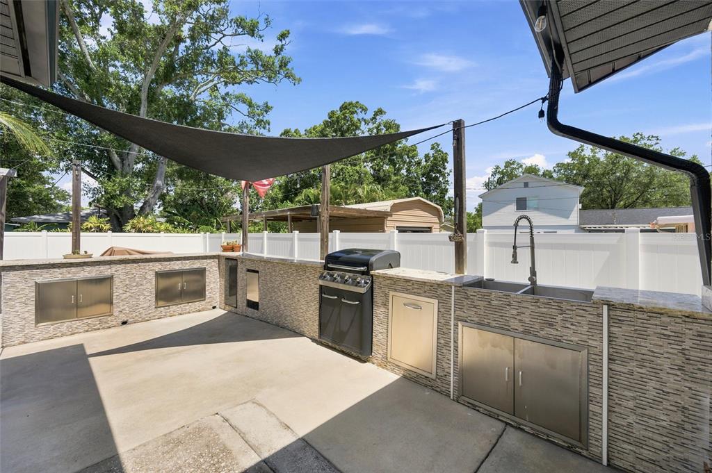 An outdoor kitchen features a stone-tiled counter, stainless steel cabinets, a grill, and a sink — 6230 CEDAR STREET NE, ST PETERSBURG, FL