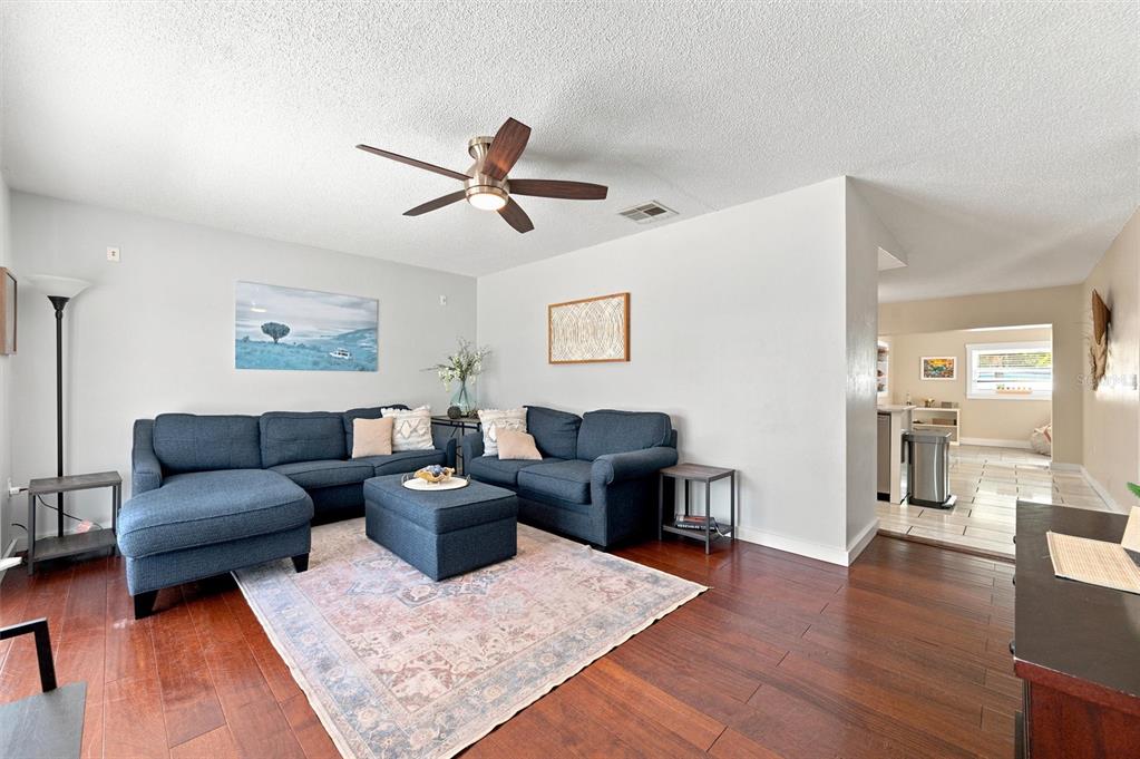 A living room features a blue sectional sofa, a patterned rug, and dark wood flooring — 6230 CEDAR STREET NE, ST PETERSBURG, FL