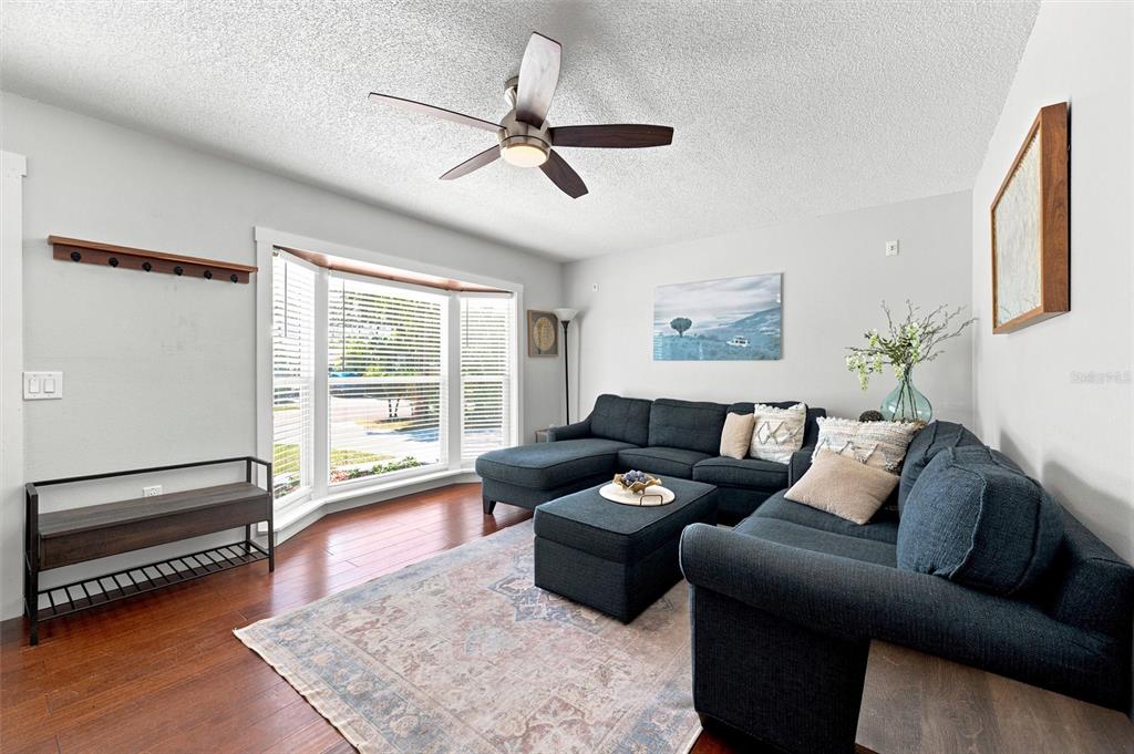 A living room features a dark blue sectional sofa, a bay window, and hardwood floors — 6230 CEDAR STREET NE, ST PETERSBURG, FL