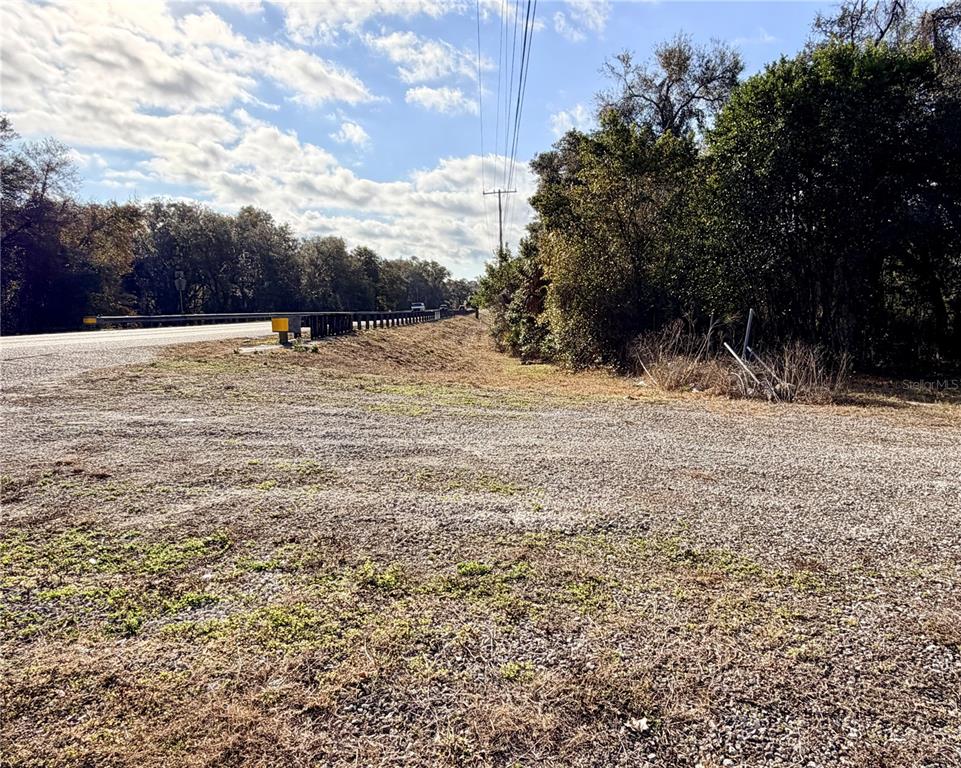 A gravel area sits beside a road with a guardrail and trees under a blue sky — 5666 S FLORIDA AVENUE, FLORAL CITY, FL