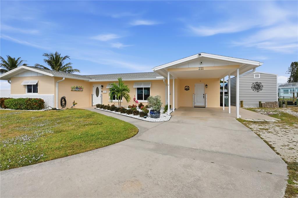 A single-story house with a light yellow exterior, a concrete driveway, and a covered carport — 211 21ST STREET NE, BRADENTON, FL