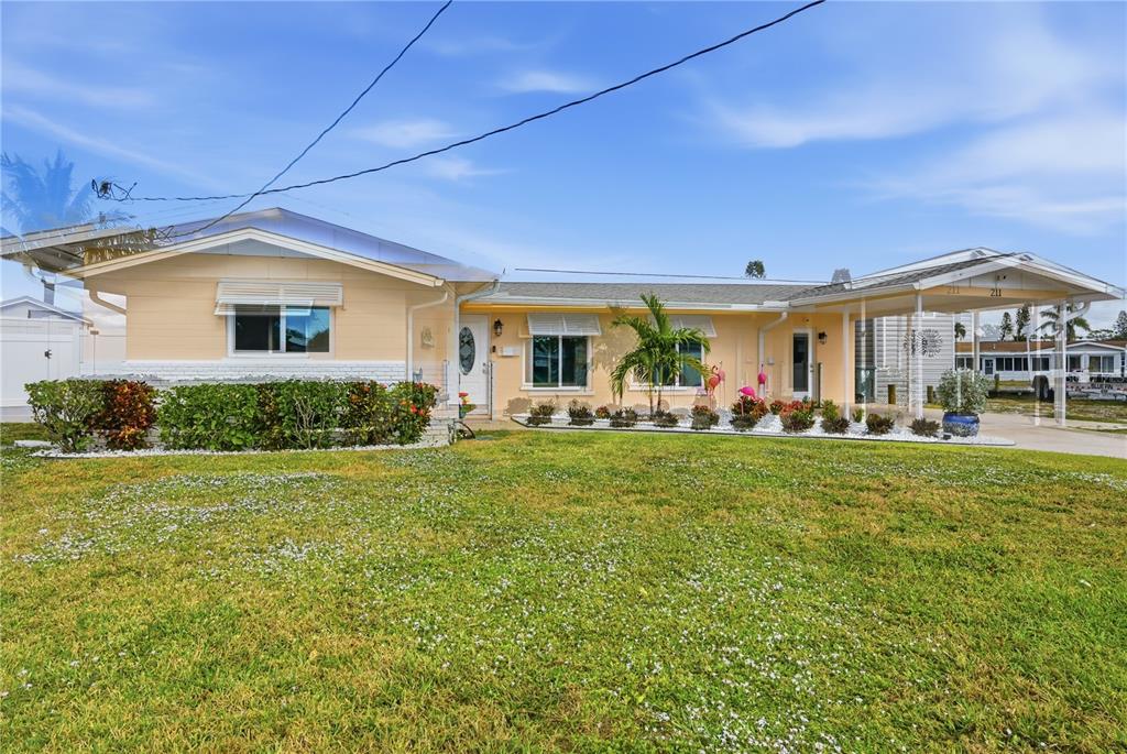 A single-story yellow house with a white brick base, a front lawn, and a carport — 211 21ST STREET NE, BRADENTON, FL