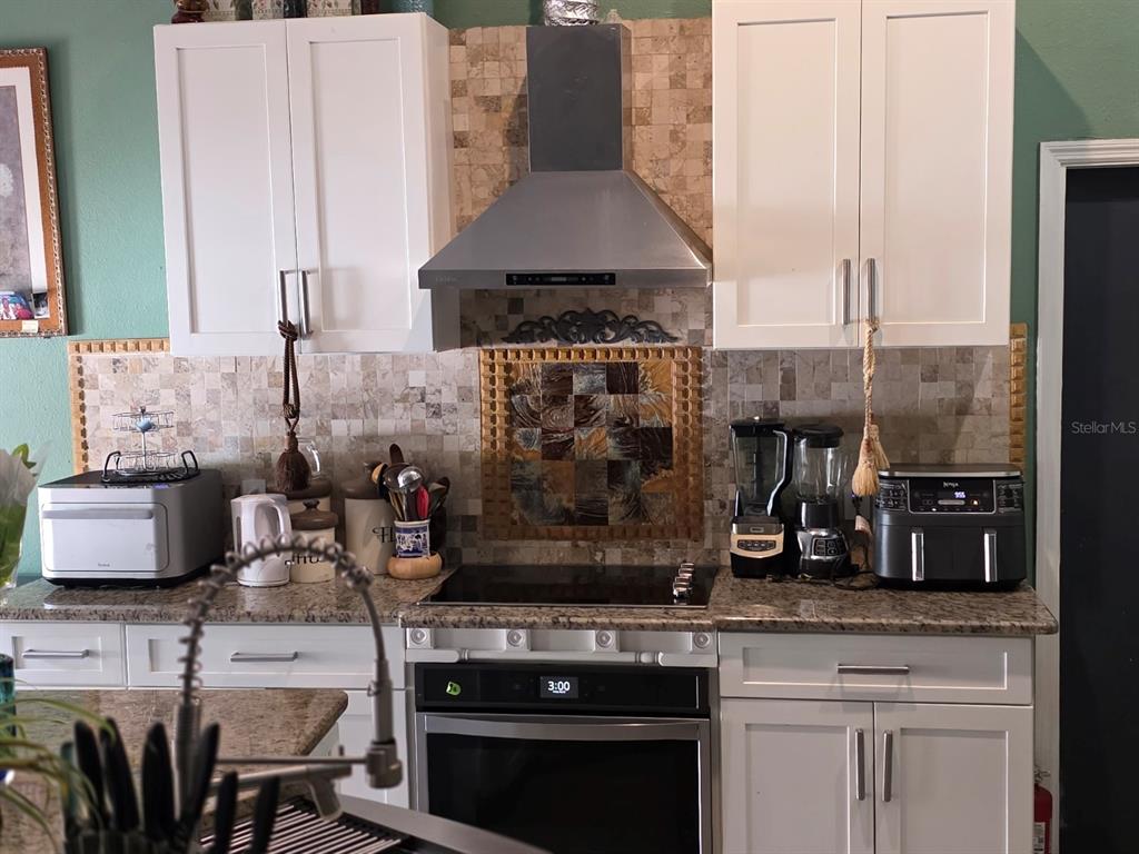 A kitchen features white cabinets, a stainless steel range hood, and a tiled backsplash — 16 PERCH DRIVE, KISSIMMEE, FL