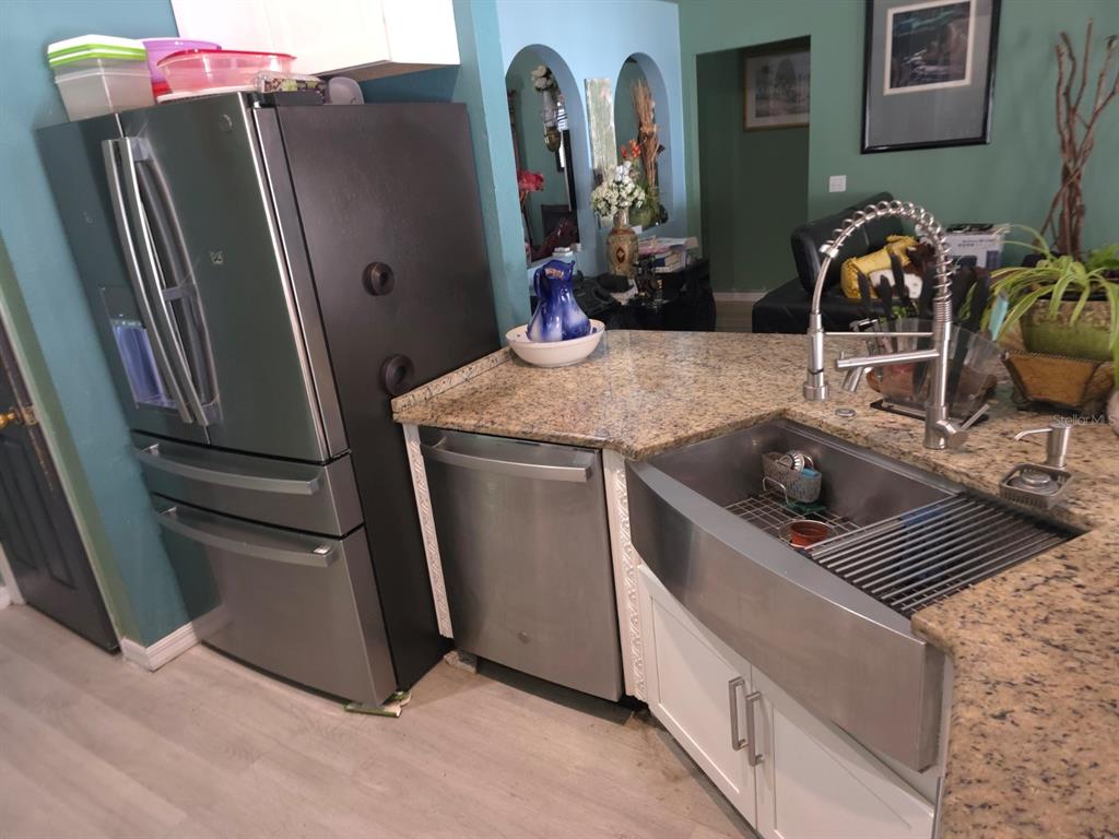 A kitchen features a stainless steel refrigerator, dishwasher, farmhouse sink, and granite countertops — 16 PERCH DRIVE, KISSIMMEE, FL