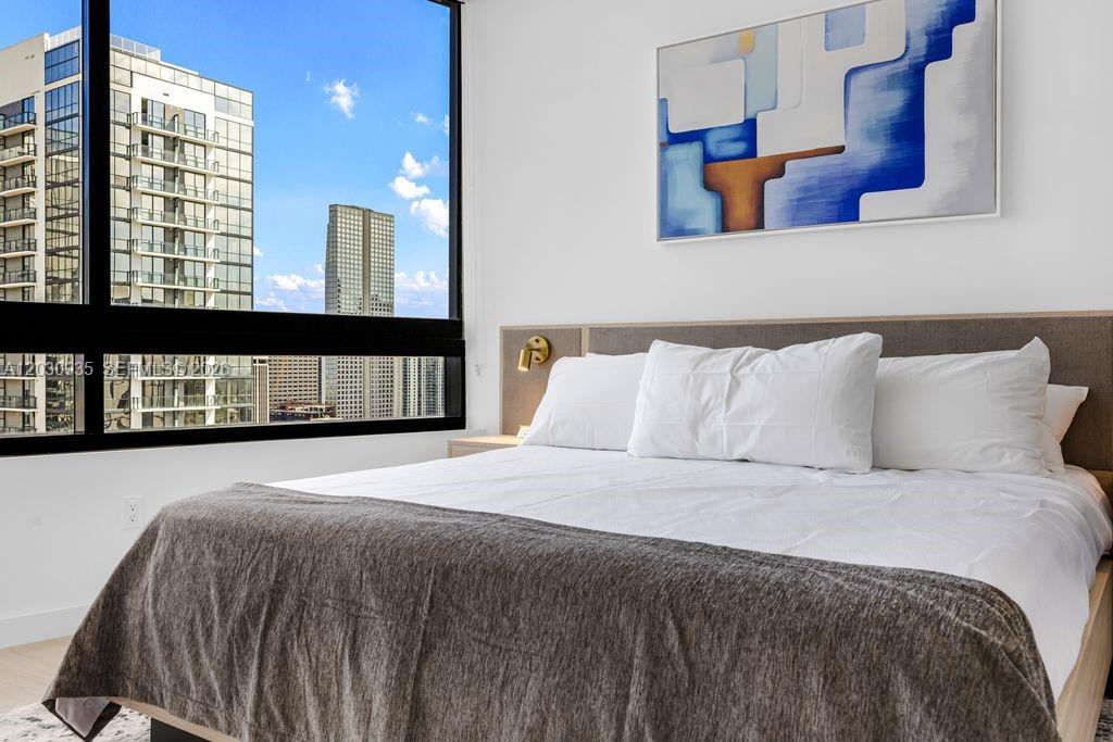 A bedroom features a bed with white linens, a gray throw, and a large window — 225 N Miami Ave # 3507, Miami FL 33128, MIAMI, FL