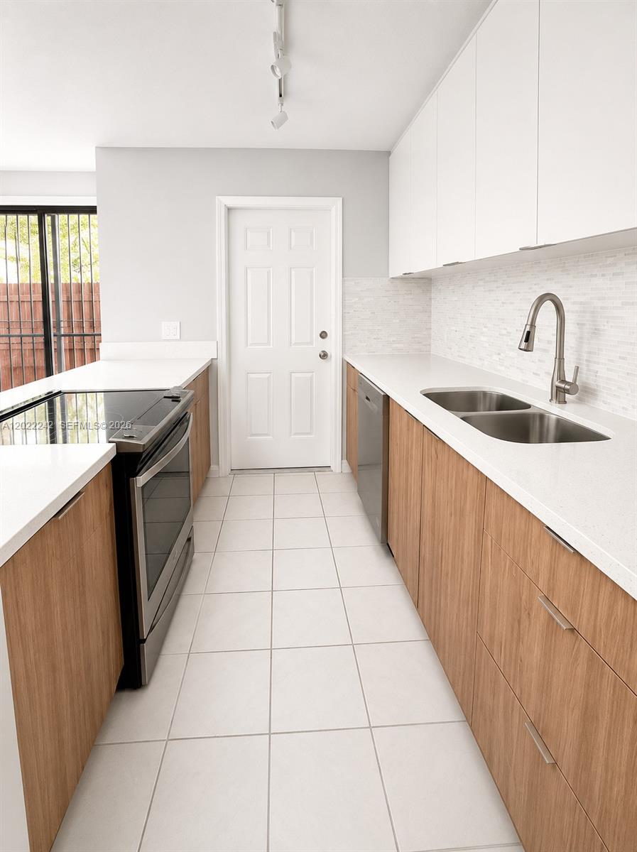 A galley kitchen features light wood cabinets, white countertops, stainless steel appliances, and tile flooring — 20033 SW 123rd Dr, Miami FL 33177, MIAMI, FL