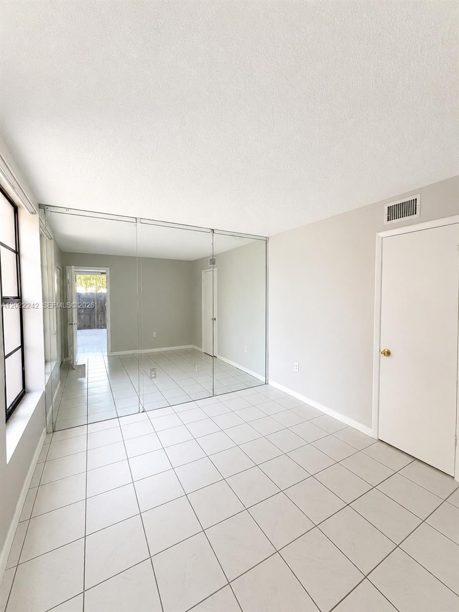A room with light-colored tile flooring, a mirrored wall, and a closed white door — 20033 SW 123rd Dr, Miami FL 33177, MIAMI, FL