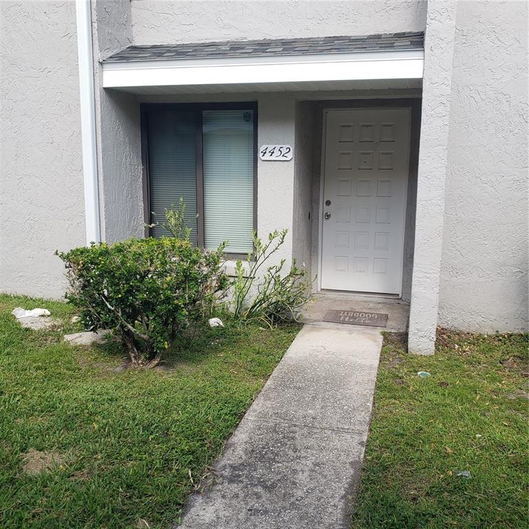 A concrete walkway leads to the white front door of a gray stucco townhouse — 4452 PINEBARK AVENUE UNIT 56-3, ORLANDO, FL