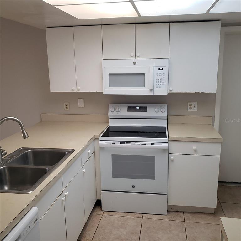 A kitchen features white cabinets, a white stove with an over-the-range microwave, and tan countertops — 4452 PINEBARK AVENUE UNIT 56-3, ORLANDO, FL