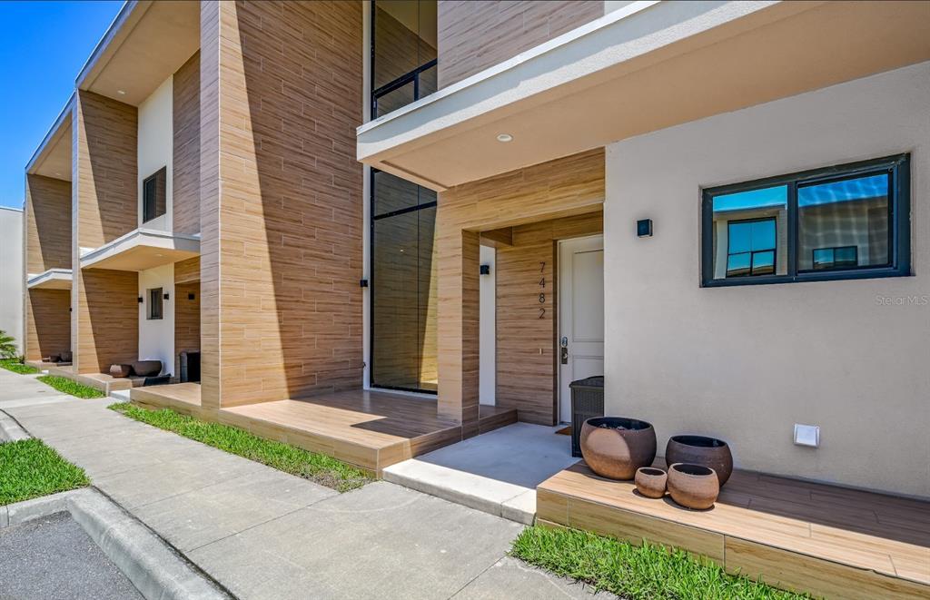 The exterior of a modern townhouse features wood-look tile siding, a glass entryway, and planters — 7482 BROOKLYN DRIVE, KISSIMMEE, FL