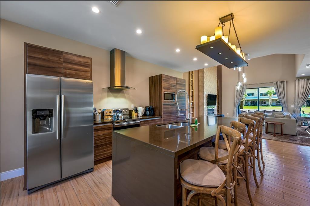 A modern kitchen features wood-grain cabinets, stainless steel appliances, a large island, and pendant lighting — 7482 BROOKLYN DRIVE, KISSIMMEE, FL