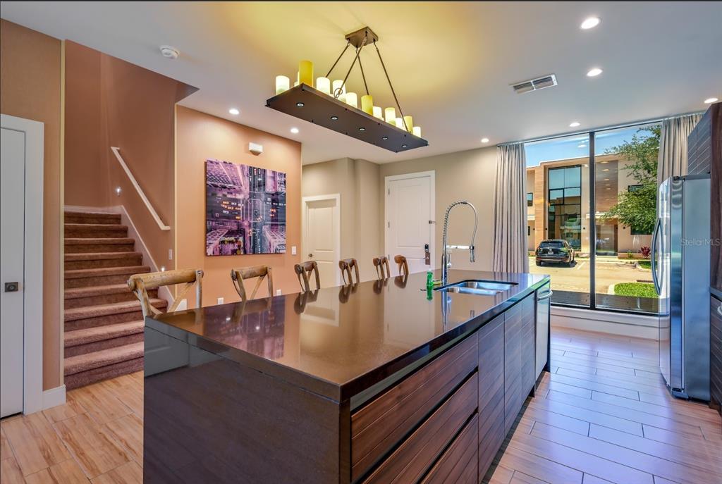 A modern kitchen features a dark wood island, stainless steel sink, and stairs leading upward — 7482 BROOKLYN DRIVE, KISSIMMEE, FL