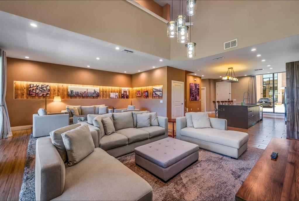 A spacious living room features light-colored sectional sofas, a central ottoman, and high vaulted ceilings — 7482 BROOKLYN DRIVE, KISSIMMEE, FL