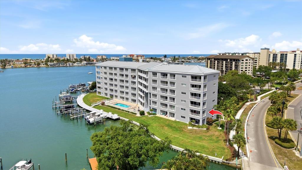 An aerial view shows a multi-story apartment building situated along a waterfront with boat docks — 610 ISLAND WAY UNIT 201, CLEARWATER BEACH, FL