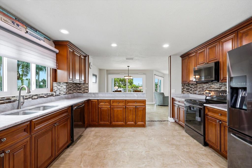 A kitchen features wood cabinets, stone countertops, tile flooring, and stainless steel appliances — 610 ISLAND WAY UNIT 201, CLEARWATER BEACH, FL