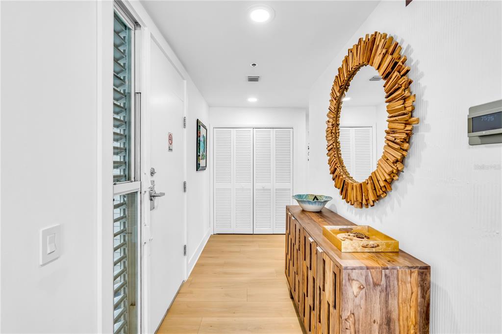 A bright entryway features light wood flooring, a wooden console table, and a sunburst mirror — 615 DREAM ISLAND PLACE UNIT 201, LONGBOAT KEY, FL