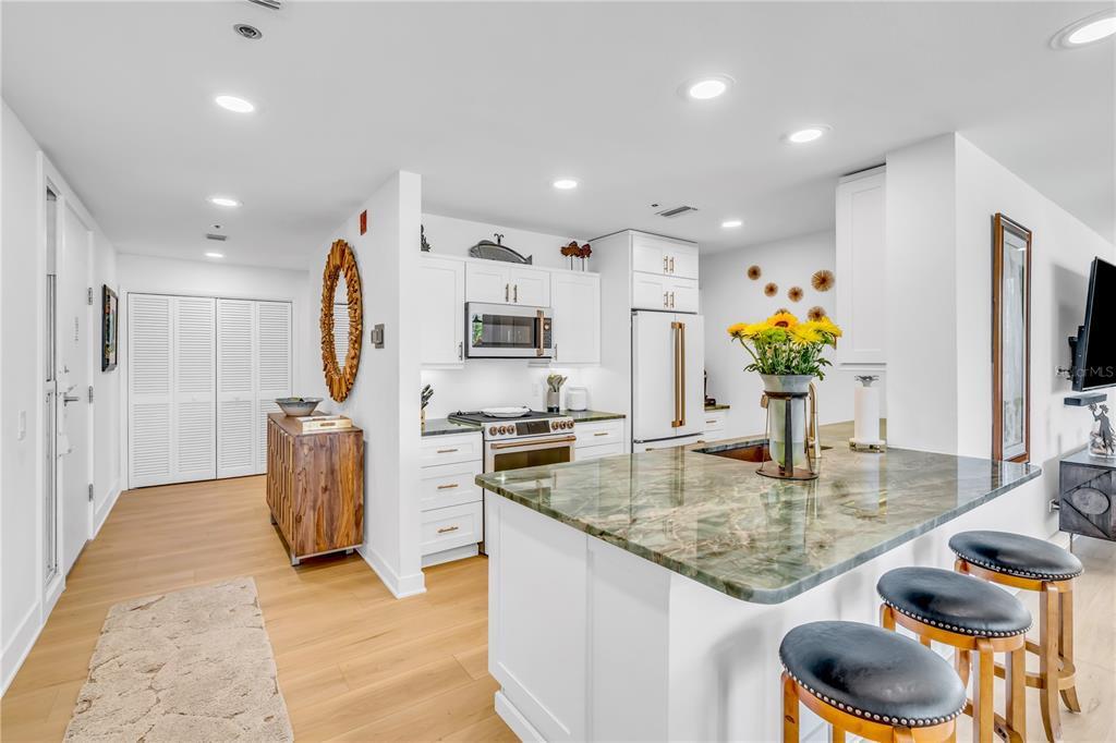 A kitchen features white cabinetry, a green stone island with bar stools, and light flooring — 615 DREAM ISLAND PLACE UNIT 201, LONGBOAT KEY, FL