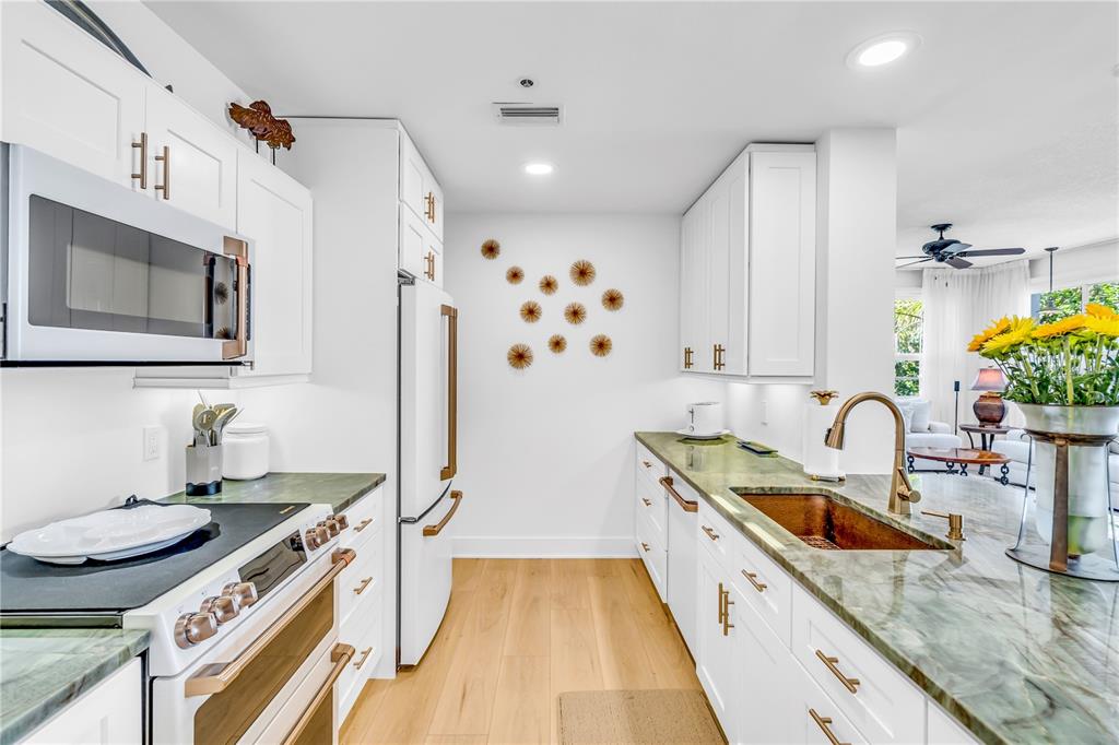 A white kitchen features green stone countertops, a copper sink, and gold-toned hardware — 615 DREAM ISLAND PLACE UNIT 201, LONGBOAT KEY, FL