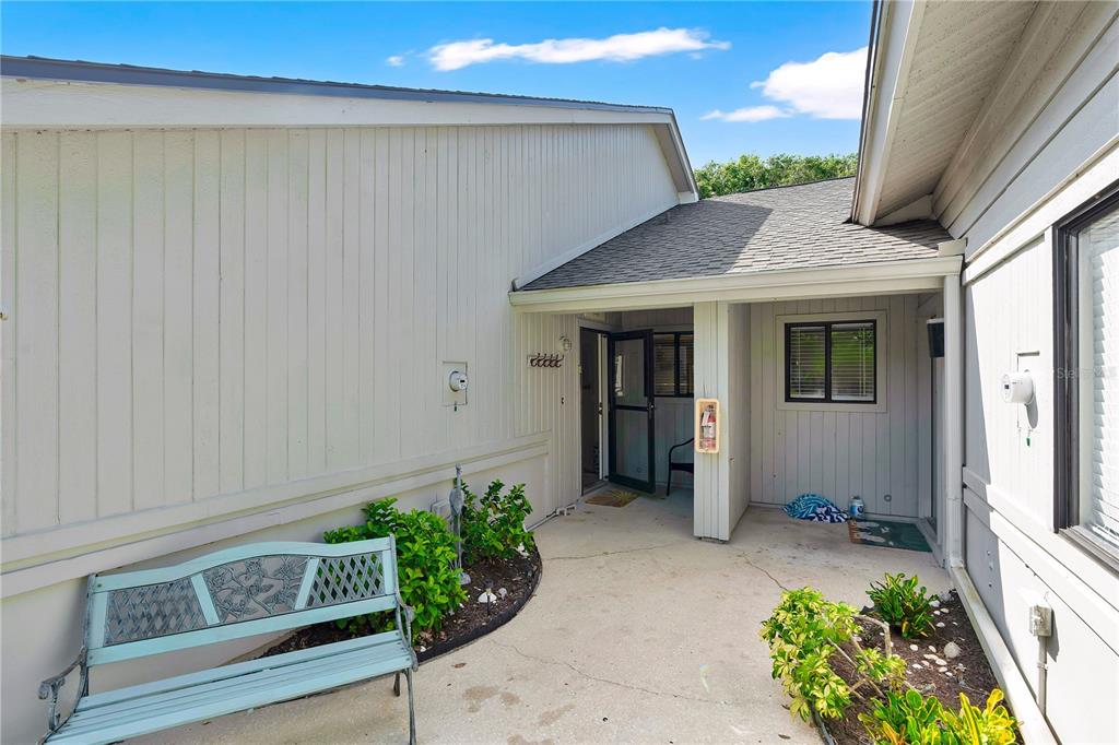 A light-colored house exterior features a concrete patio, a metal bench, and an entryway — 4360 SEA MIST DRIVE, NEW SMYRNA BEACH, FL