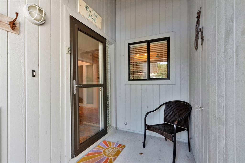 A covered porch features vertical gray siding, a glass storm door, a window, and a chair — 4360 SEA MIST DRIVE, NEW SMYRNA BEACH, FL