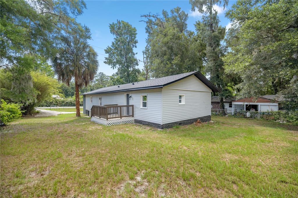 The exterior of a light gray, single-story house features a wooden deck and a yard — 1127 SW 140TH AVENUE, OCALA, FL