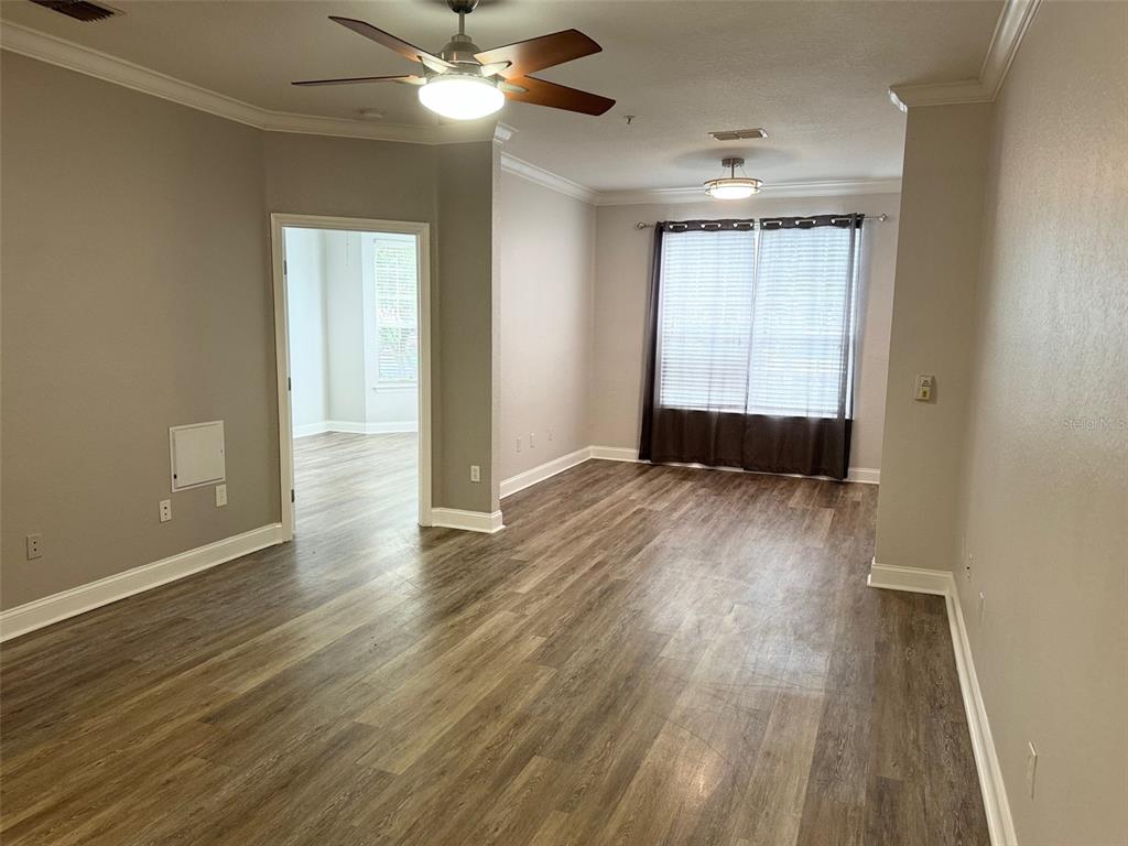 An empty room features wood-look flooring, a ceiling fan, and a window with dark curtains — 3367 S KIRKMAN ROAD UNIT 1111, ORLANDO, FL
