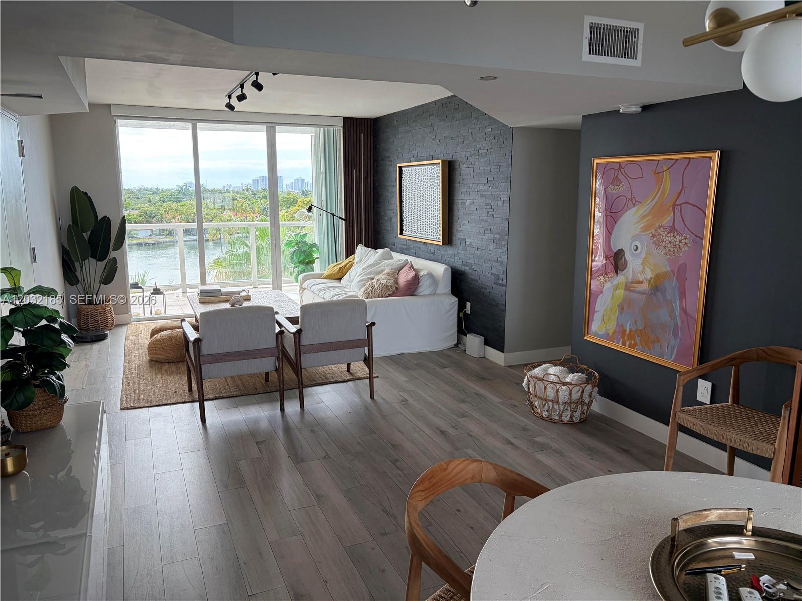 A modern living room features a stone accent wall, a large parrot painting, and balcony views — 5900 Collins Ave # 702, Miami Beach FL 33140, MIAMI BEACH, FL