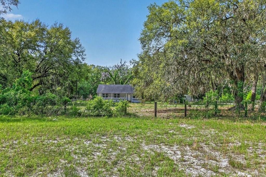 A small, single-story house sits in a grassy field surrounded by large, moss-covered oak trees — 461 OLD STARKE ROAD, PALATKA, FL