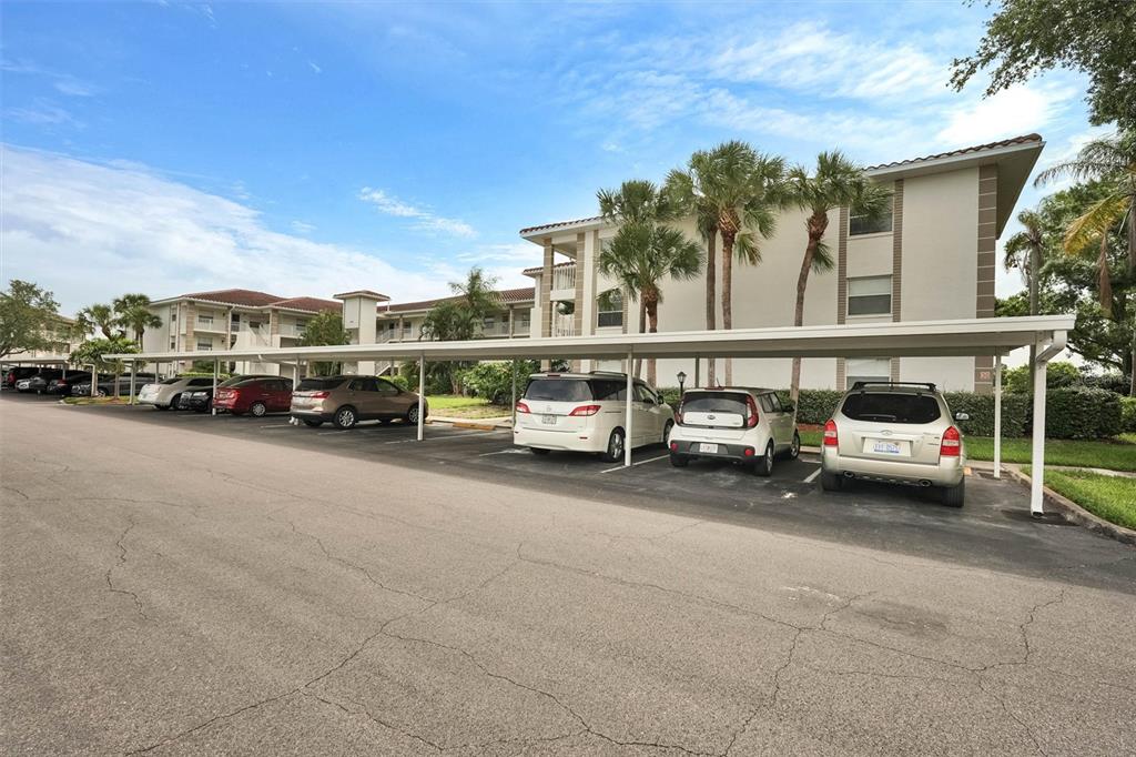 A multi-story apartment building with a covered parking area featuring several parked cars — 6507 STONE RIVER ROAD UNIT 102, BRADENTON, FL
