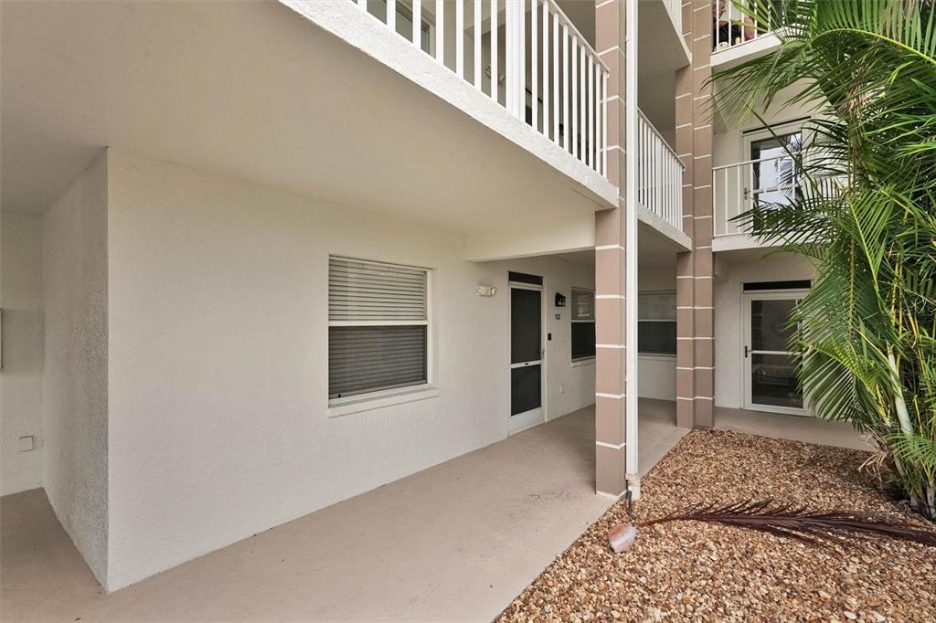 A ground-level apartment entrance with a screened door, white stucco walls, and a gravel yard — 6507 STONE RIVER ROAD UNIT 102, BRADENTON, FL