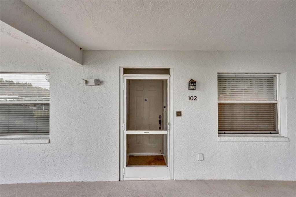 The exterior entrance of a residential unit features a white door, screen door, and windows — 6507 STONE RIVER ROAD UNIT 102, BRADENTON, FL