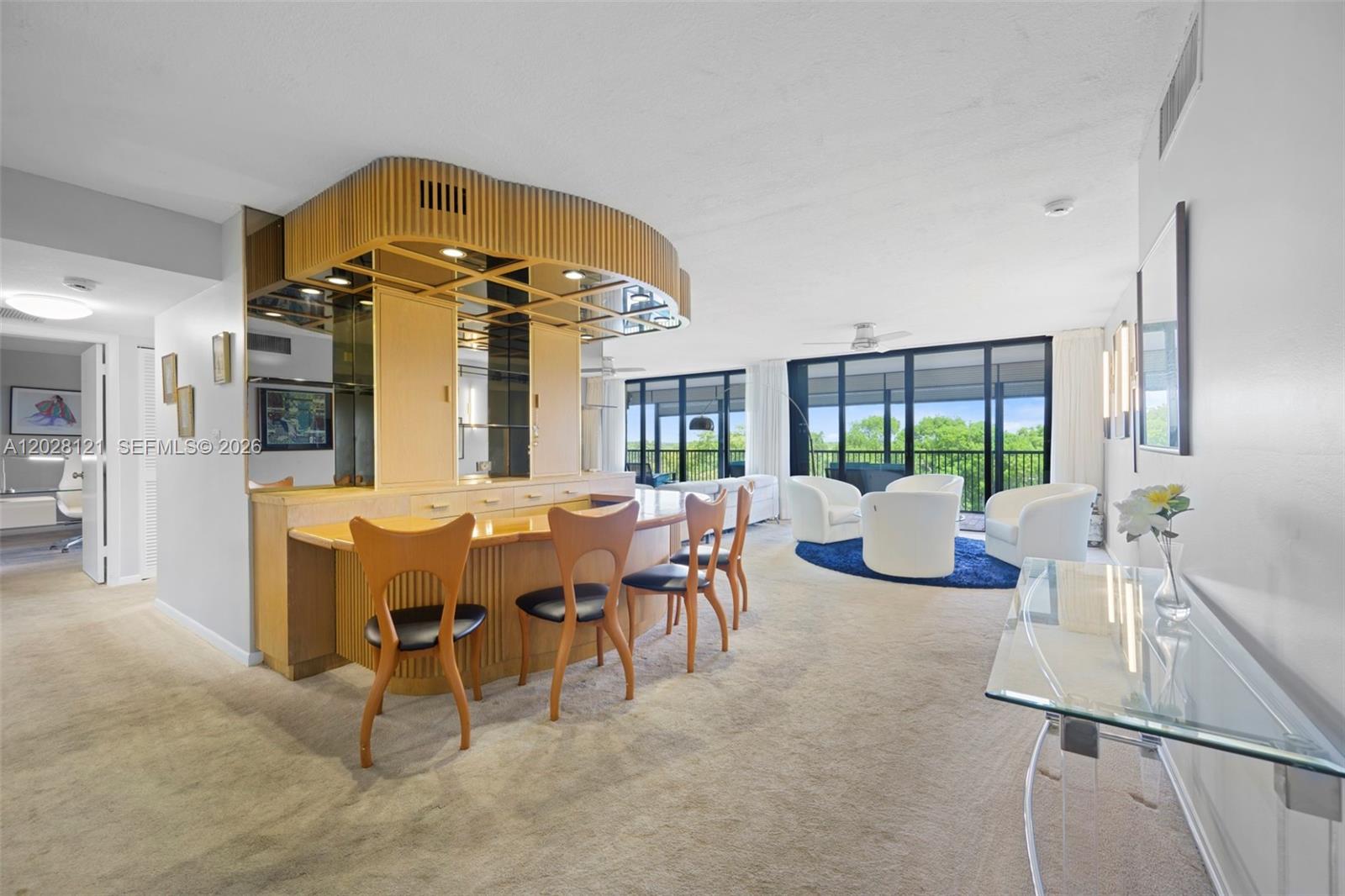 A living room features a built-in wooden bar, mid-century style chairs, and floor-to-ceiling windows — 2804 N 46th Ave # C630, Hollywood FL 33021, HOLLYWOOD, FL