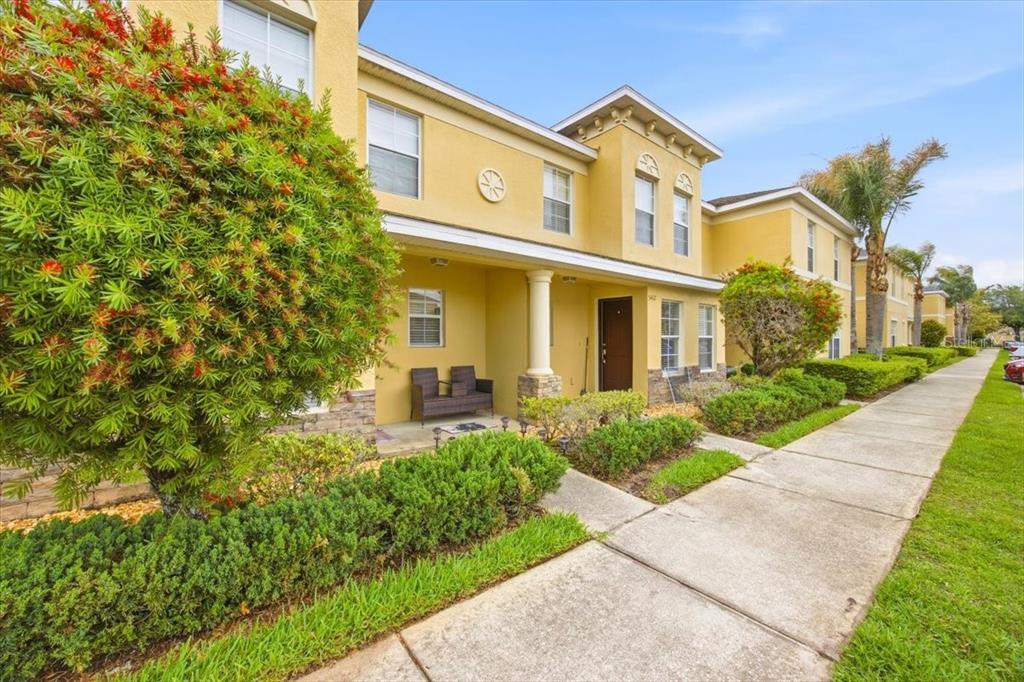 A two-story yellow townhouse with a covered entryway, stone accents, and a landscaped front yard — 5410 QUARRY ROCK ROAD, LAKELAND, FL