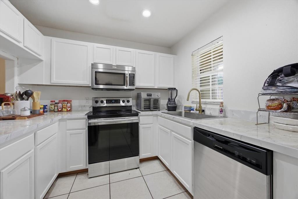 A kitchen features white cabinets, stainless steel appliances, and white marble-look countertops — 5410 QUARRY ROCK ROAD, LAKELAND, FL