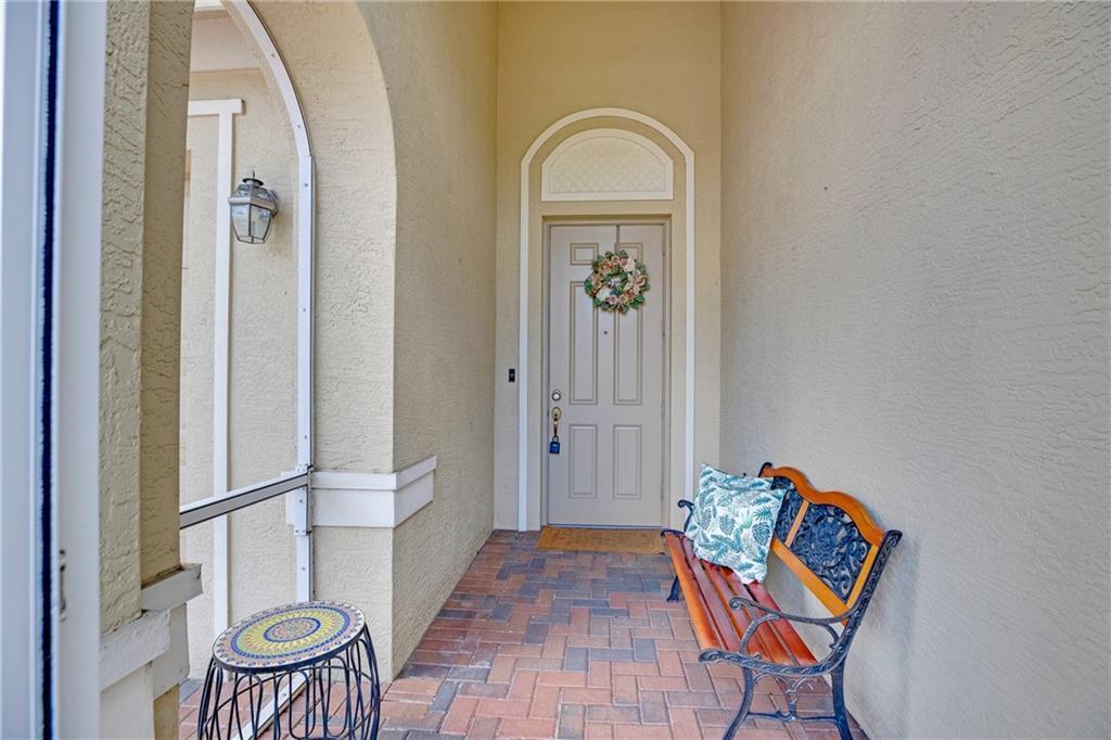 A covered entryway features a brick floor, a wooden bench, and a front door — VERO BEACH, FL