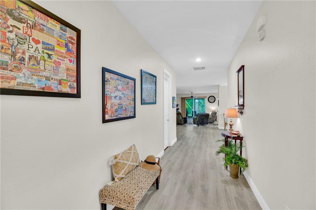 A hallway with light wood-look flooring leads to an open living area with a patio — VERO BEACH, FL