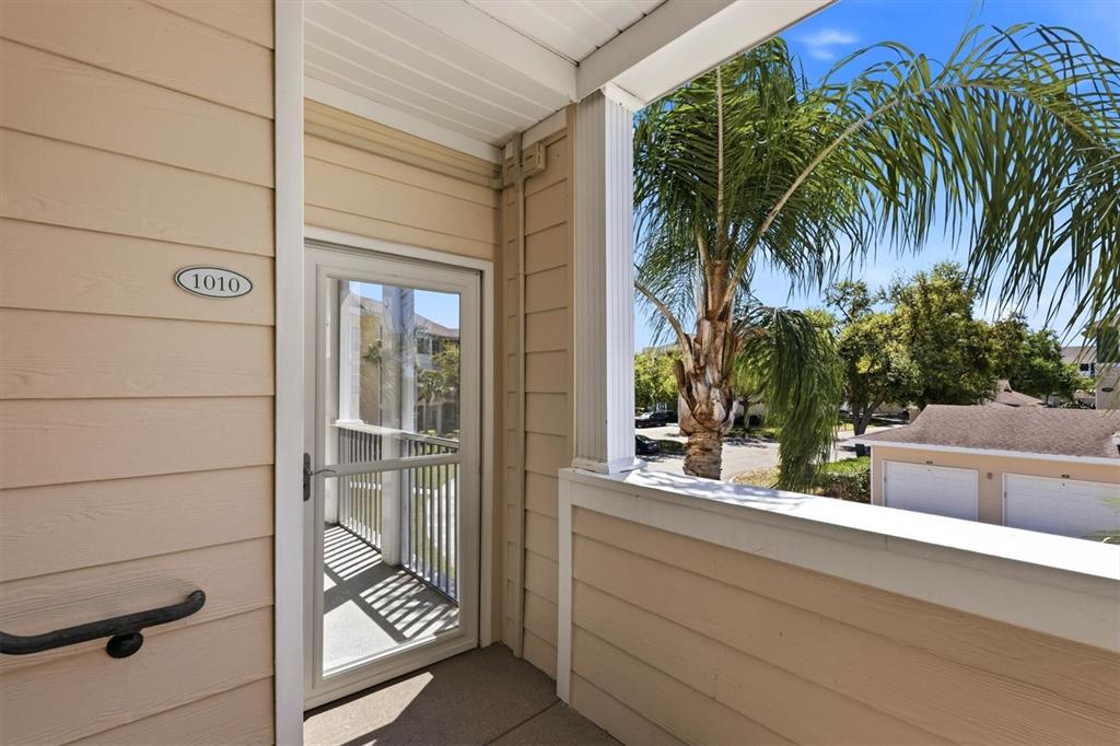 An exterior balcony features tan siding, a white door labeled 1010, and a palm tree view — 4802 51ST STREET W UNIT 1010, BRADENTON, FL
