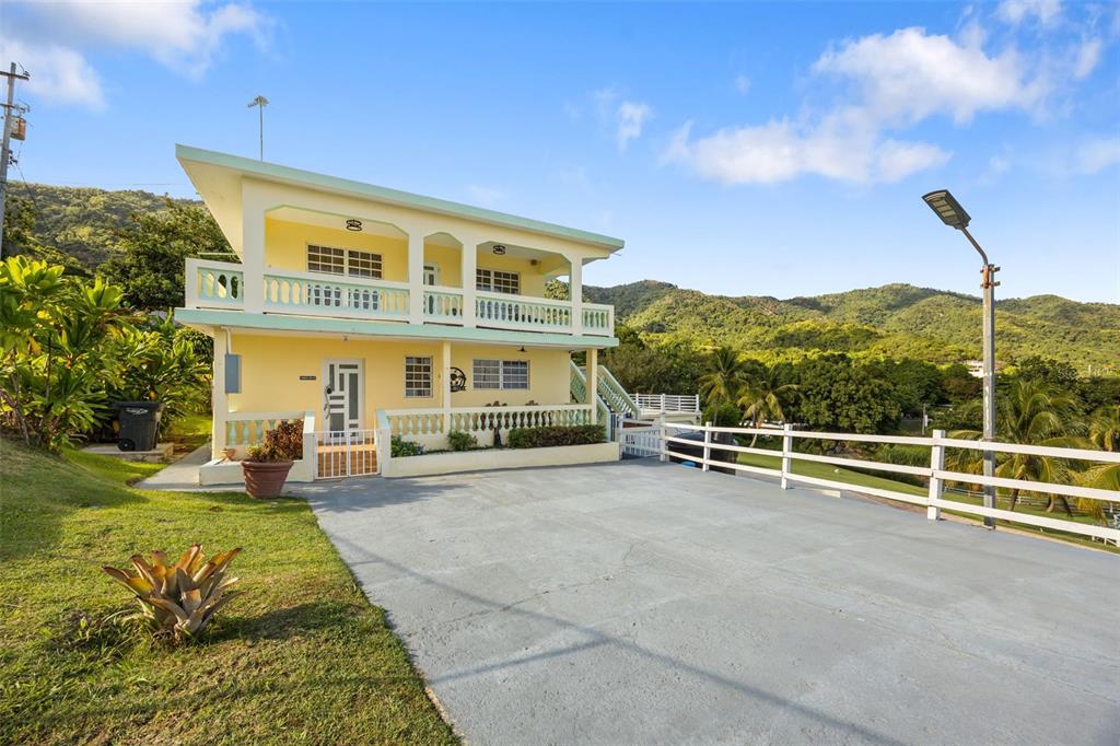A two-story yellow house with a balcony and a concrete driveway sits against mountains — Carr 3 CAMINO COOPERATIVO, PATILLAS, PR
