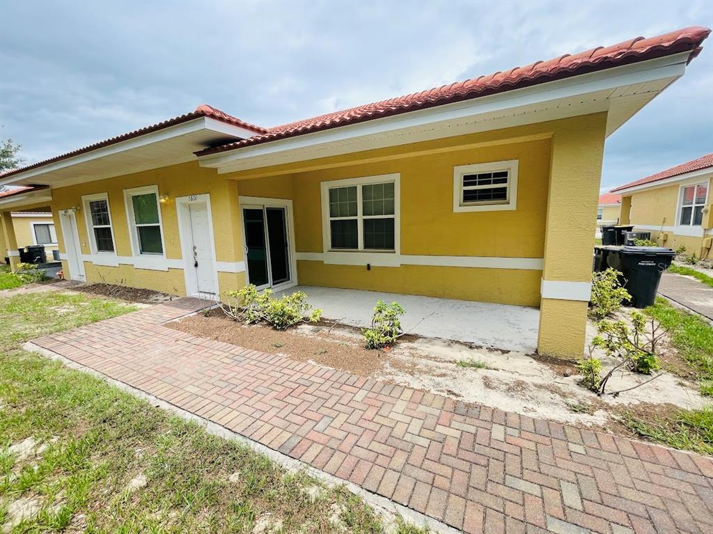 A yellow stucco house exterior features a red tile roof, covered patio, and brick walkway — 1601 CUMIN DRIVE, KISSIMMEE, FL